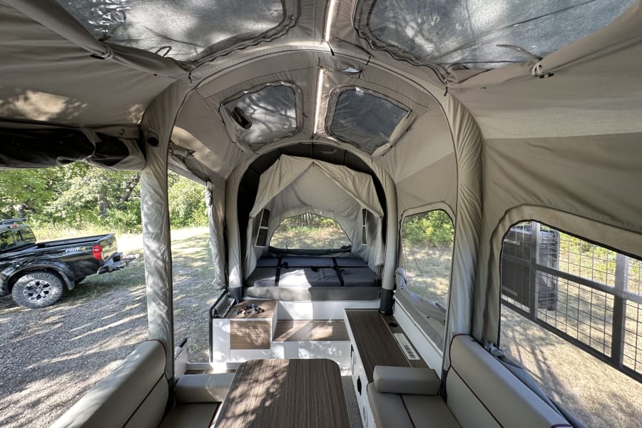 Inside a modern pop-up rv rental: bed, dining area, and panoramic windows.