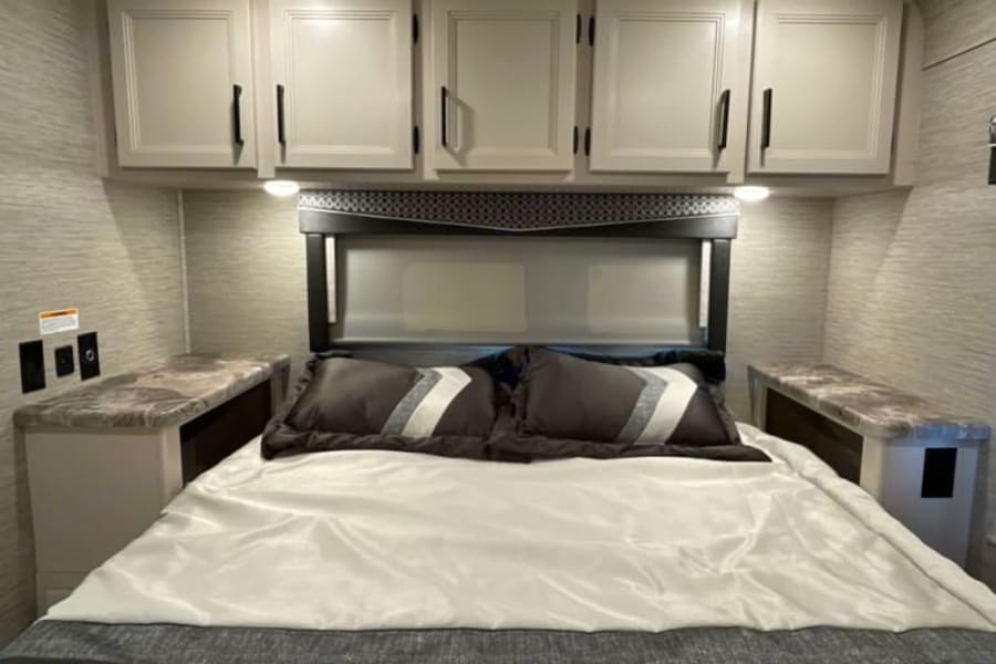 This RV rental features a comfortable bedroom with overhead storage, bedside tables, and a large bed, perfect for your next trip.