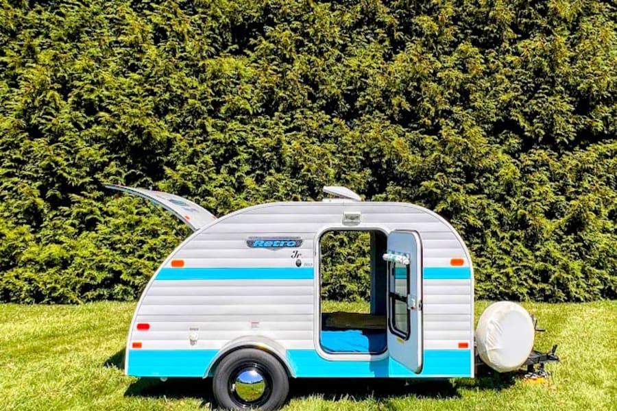 This charming white & blue Retro Jr. teardrop camper, ideal for RV rental, sits on a vibrant green lawn under blue skies.