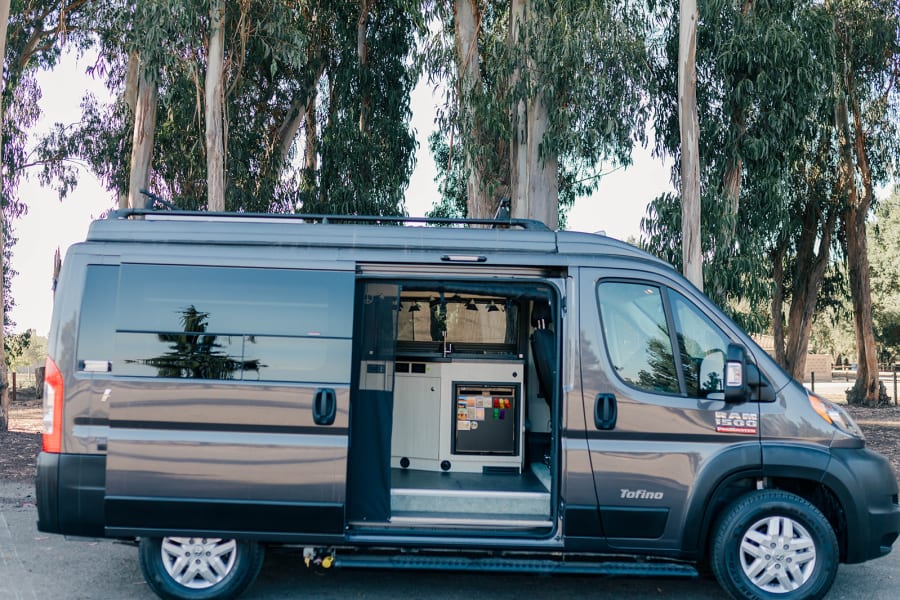 Spacious gray camper van, ideal for RV rental. Side door open shows interior kitchenette with sink & fridge.