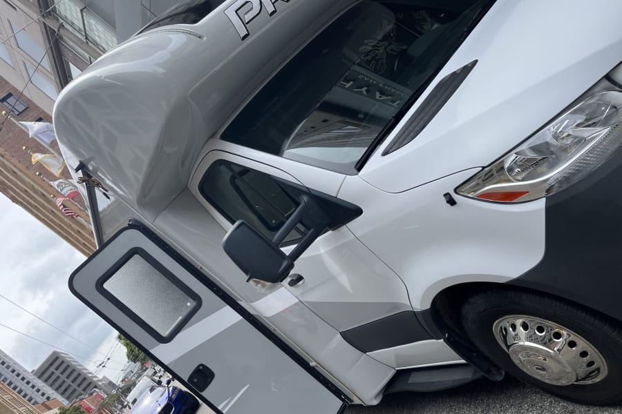 White Thor Motor Coach Prism RV rental parked on a city street, entry door open. Features sleek design with gray accents.