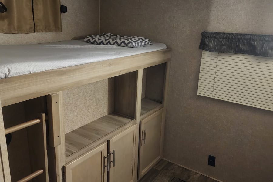 RV rental interior features a sturdy bunk bed with a ladder, ample storage cabinets, and a window with blinds.