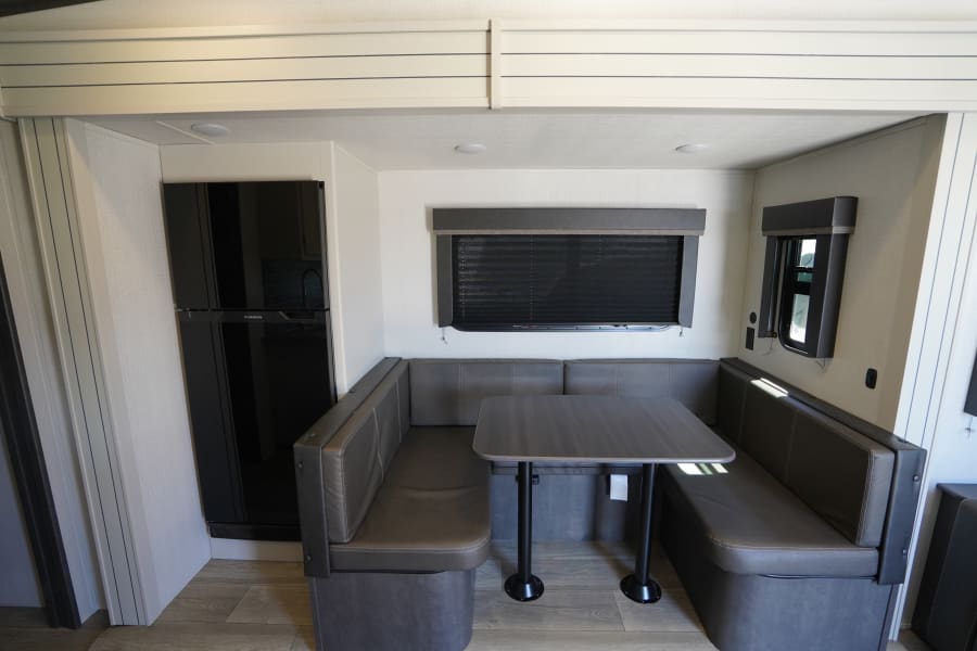 RV rental interior featuring a spacious dinette with gray seating, a table, and a large black refrigerator. Ideal for travel.