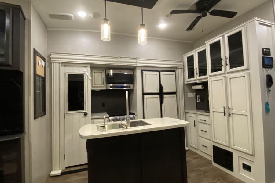 Modern RV rental kitchen interior with island sink, integrated appliances, and spacious white cabinetry.