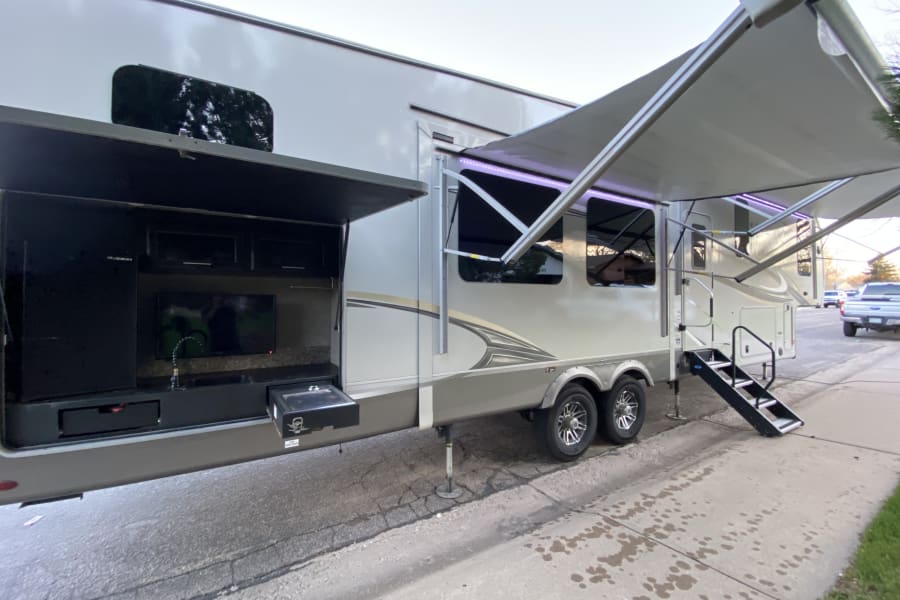 Spacious fifth-wheel RV rental with outdoor kitchen, TV, lighted awning, and steps for adventures.