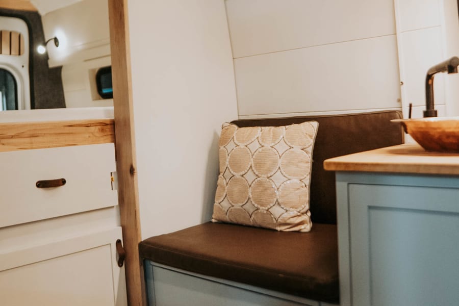 Cozy RV rental interior showcasing built-in seating, light blue kitchenette, and warm wooden accents for comfortable travel.