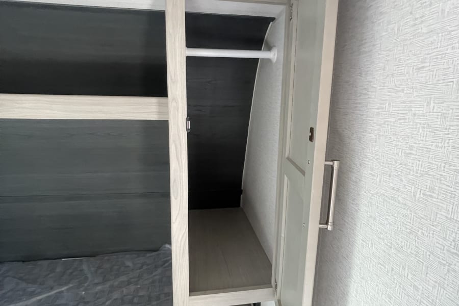Inside an RV rental, showing an open wardrobe with a hanging rod above a bed, ready for your travel essentials.
