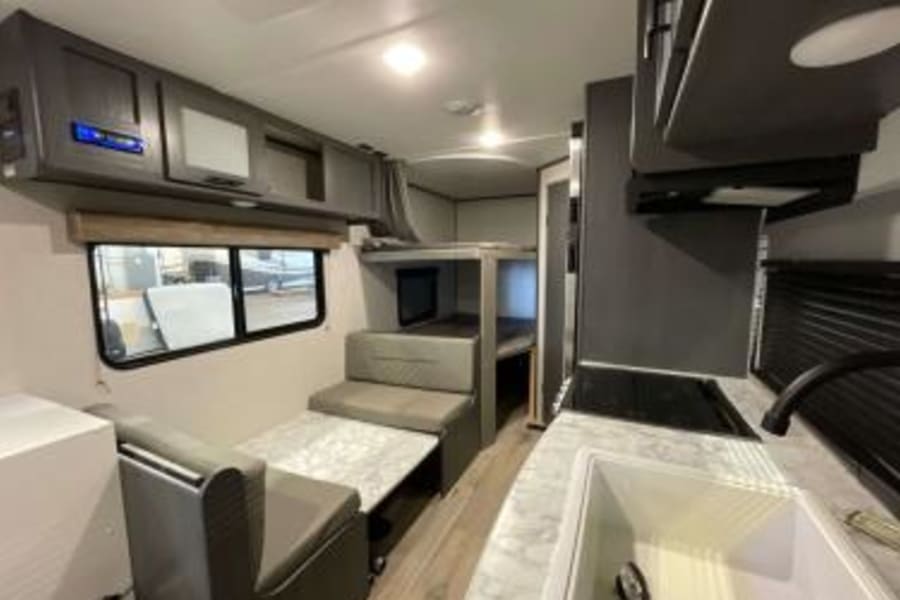 RV rental interior: The inside of a travel trailer shows a kitchen, dinette area, and bunk beds for travelers.