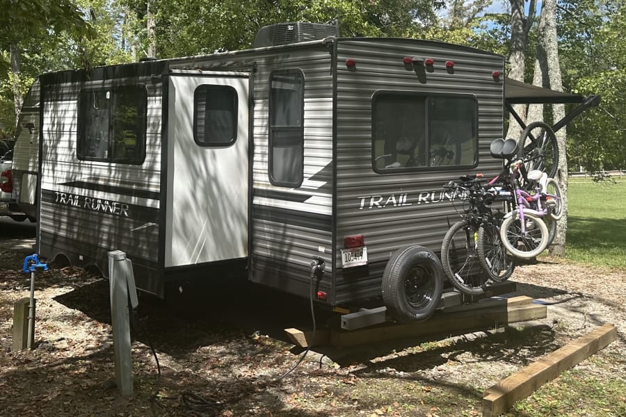 Ready for adventure: This Trail Runner RV rental, equipped with bikes, is perfectly set up at a shaded campsite.