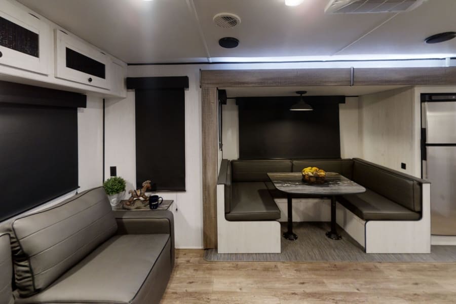 RV rental interior featuring a comfortable gray sofa, a U-shaped dinette with a table, and a kitchen area.