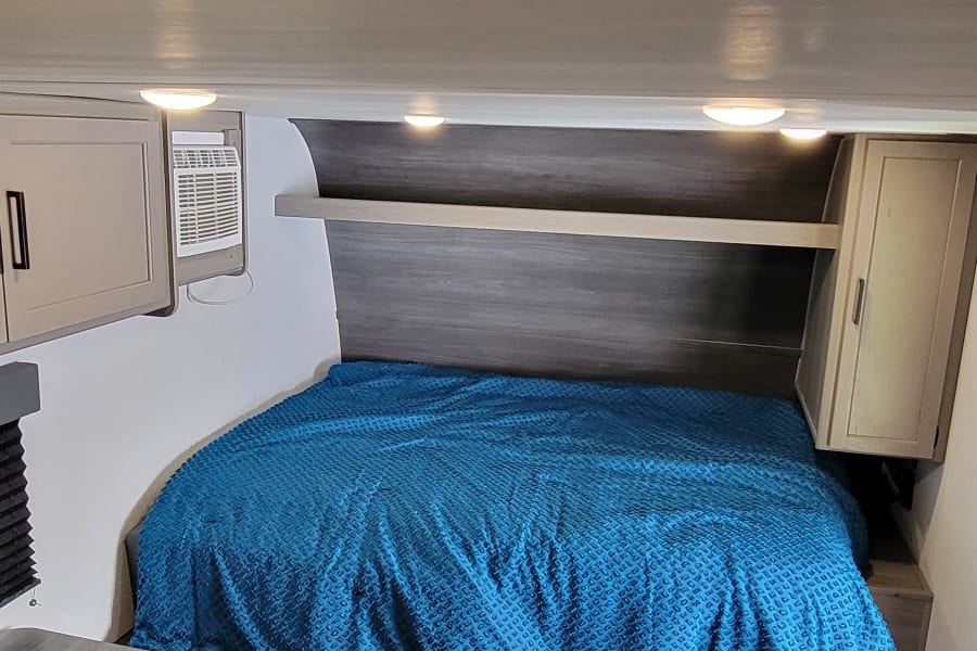 Inside an RV rental: a comfortable bed, dinette, kitchen area, and a colorful rug on the floor.