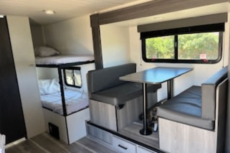 Explore this comfortable RV rental interior, featuring bunk beds and a dinette. Perfect for family adventures.