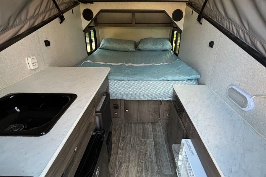Inside an RV rental, featuring a comfortable bed, kitchenette with sink, fridge, and AC unit for your adventure.