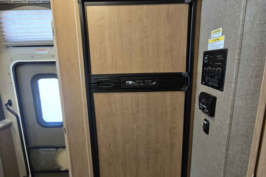 Inside this RV rental: a built-in wood-paneled refrigerator, cabinet, and control panel beside the entry steps.