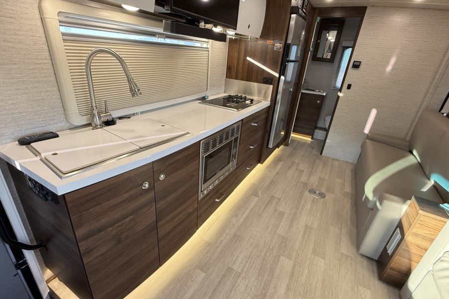 Modern RV rental interior with compact kitchen, full appliances, and comfortable lounge seating. Ideal for road trips.