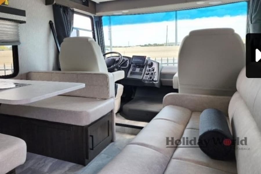 Spacious RV rental interior with comfortable dining and lounge areas, plus the driver's cockpit. Ideal for travel comfort.