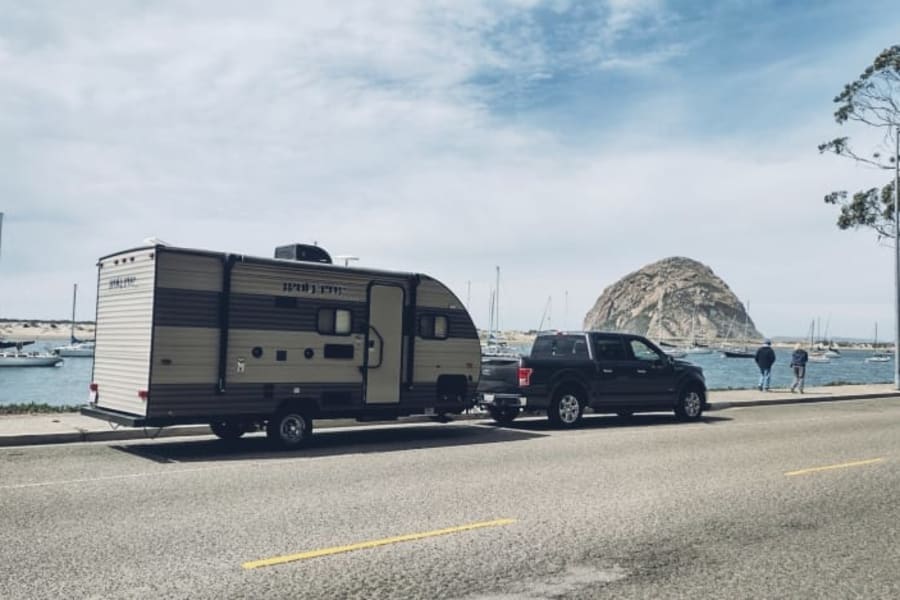 Scenic **RV rental** by Morro Bay: Truck towing a travel trailer, with sailboats and the iconic Morro Rock.
