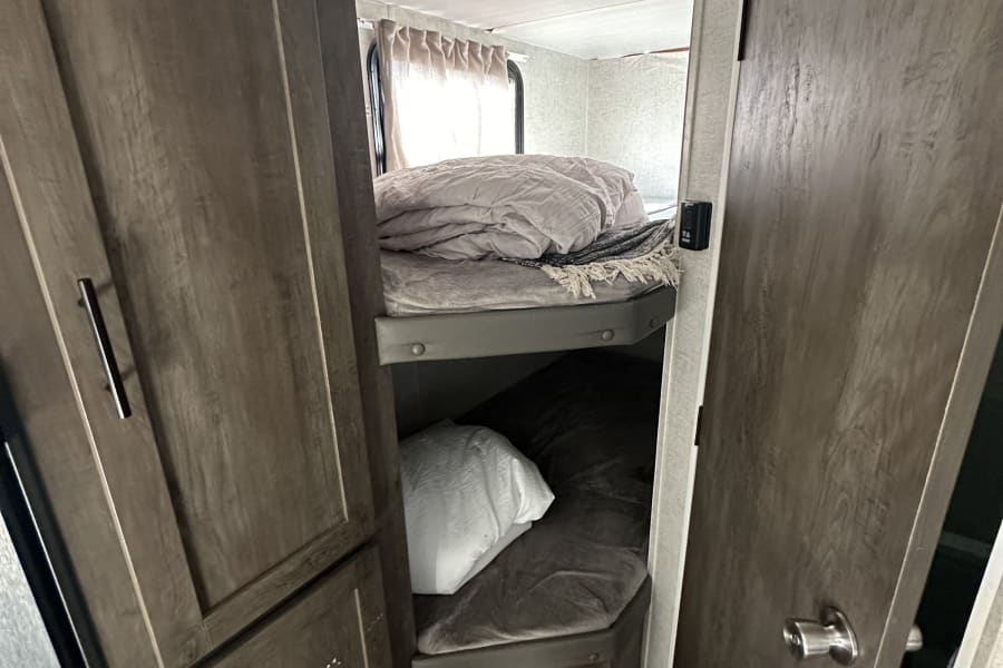 An RV rental interior reveals stacked bunk beds, upper made with a light duvet, lower with a darker blanket. Compact and practical.