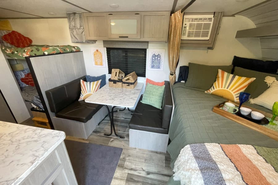 Cozy RV rental interior with dinette, main bed, and bunk for a comfortable travel experience.