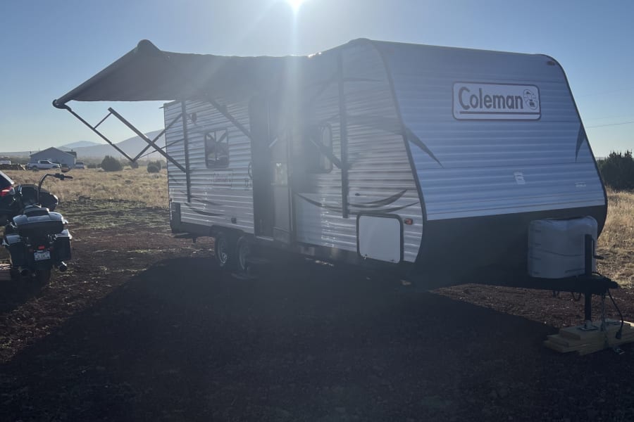 Coleman RV rental with awning extended in sunny outdoors. A motorcycle is parked. Ideal for camping & outdoor travel.