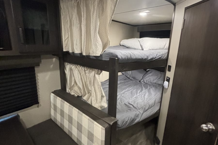 RV rental interior: cozy bunk beds with privacy curtains and a functional dinette, ideal for family trips.
