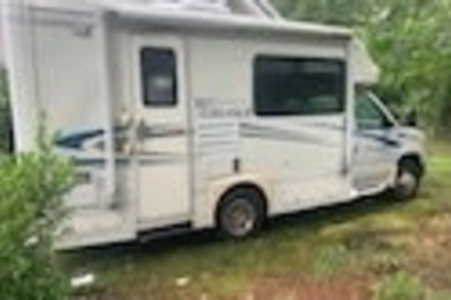 White Class C RV rental with extended awning, parked on grass. Ideal for travel and outdoor adventures.