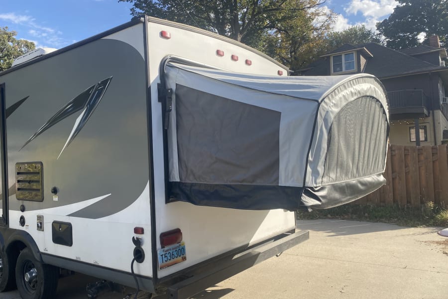 RV rental: A grey and white expandable travel trailer, with its rear pop-out tent extended, parked on pavement.