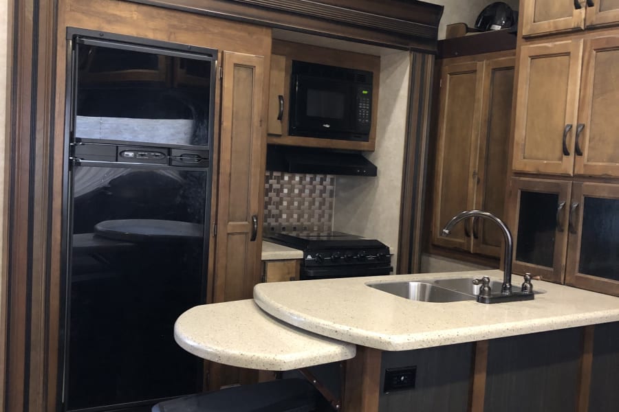 RV rental kitchen: modern interior with black appliances, light counters, island sink, and wood cabinets.