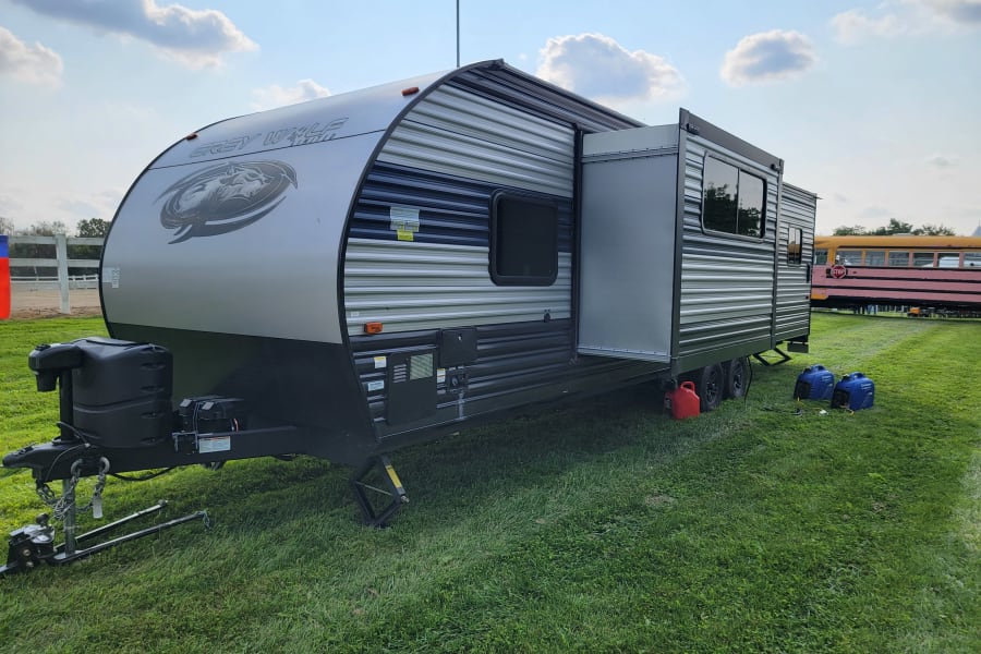 Grey Wolf travel trailer (RV rental) with slide-out extended, parked on grass with generators.