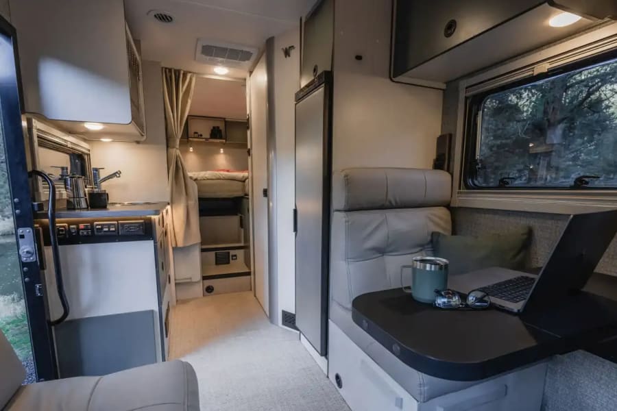 Step inside this modern rv rental, revealing a functional kitchen, comfortable lounge with laptop, and rear bunk beds.