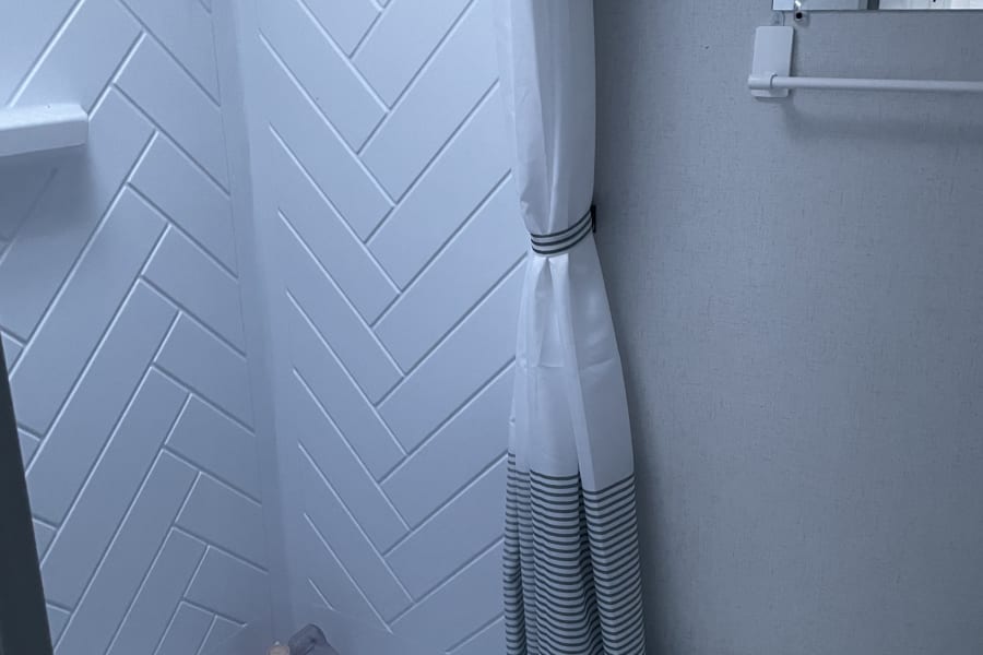 RV rental bathroom: compact design with white herringbone shower, essential toilet, and tied-back curtain for travel comfort.