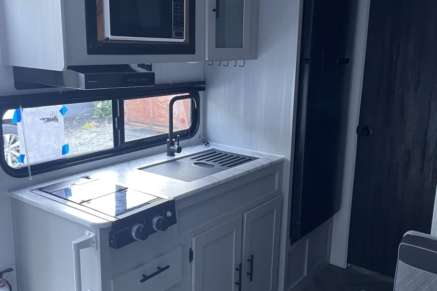 Modern RV rental kitchen with microwave, Greystone stove, sink, fridge, cabinets, and herringbone flooring visible.