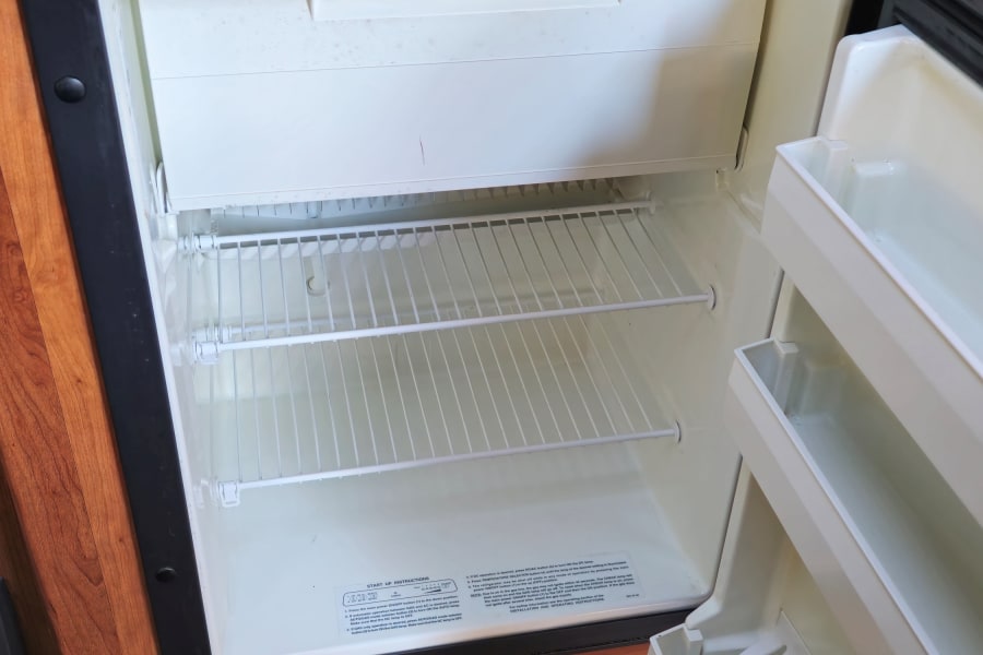 RV rental refrigerator, open and empty. Control panel shows temp settings (cold to coldest) and power options (ON/OFF, DC/AC/Gas).