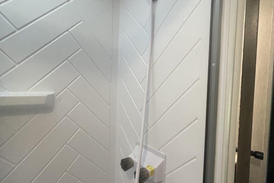 A practical shower inside an RV rental, featuring white herringbone walls, a handheld shower, and faucet controls.