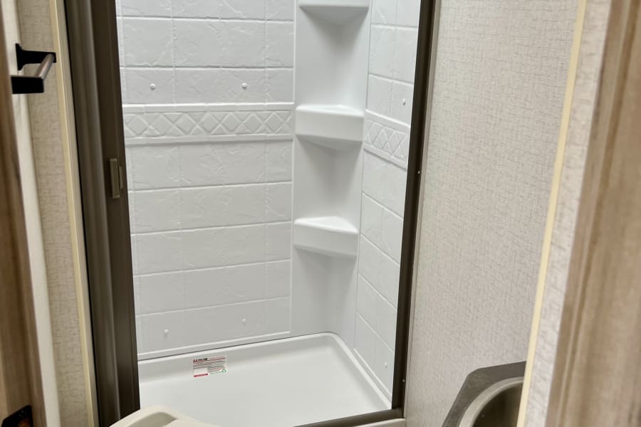 This compact RV rental bathroom features a functional shower, toilet, sink, and wall hooks for convenience.