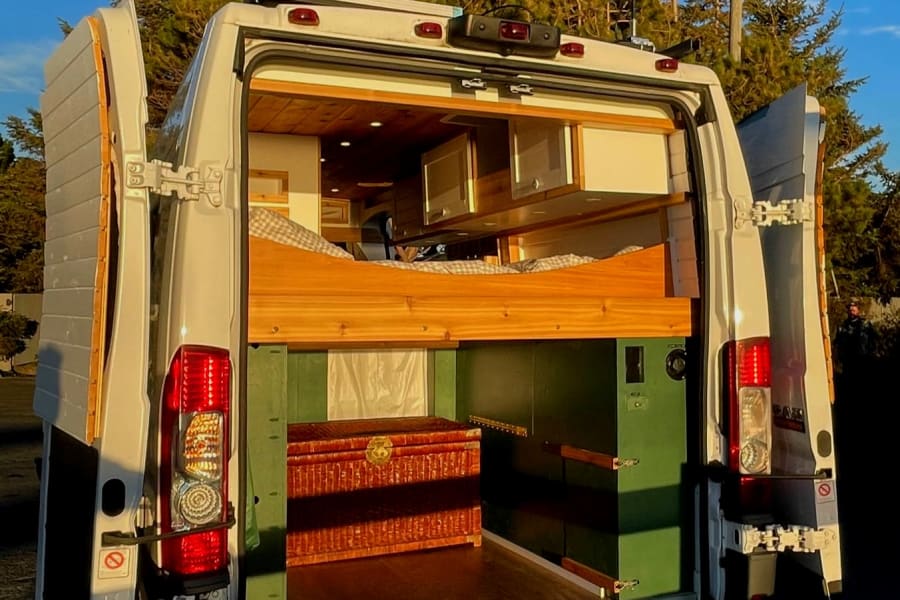 Open RV rental van's rear reveals a custom wood interior with a raised bed and lower storage for travel.