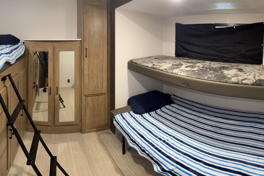 This RV rental interior features multiple bunk beds, a ladder, blue and white striped bedding, and mirrored storage.