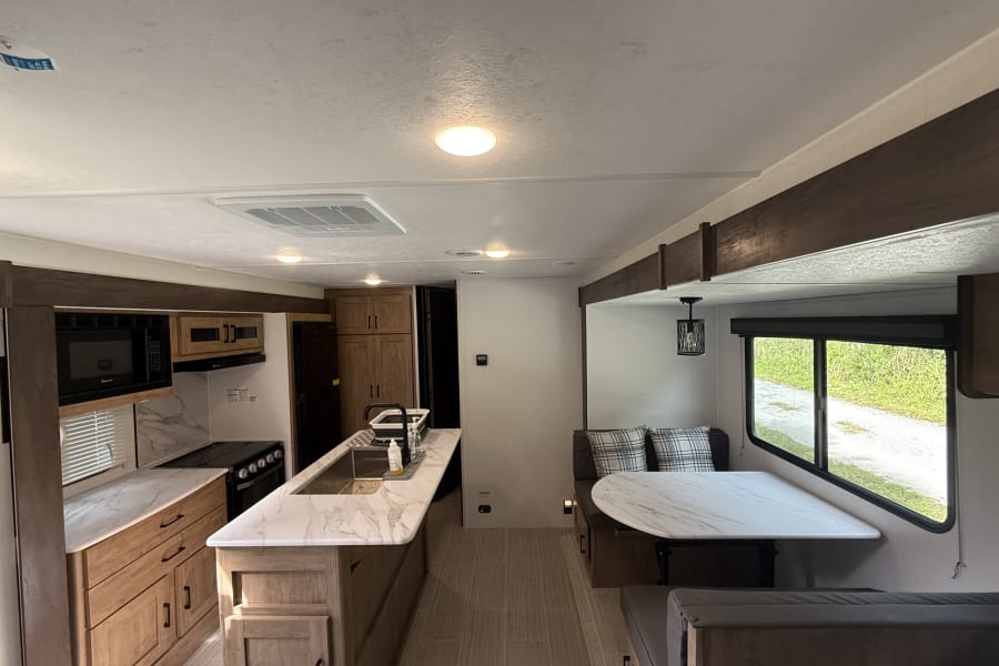 Inside a bright RV rental: a sleek kitchen with an island and modern appliances, plus a cozy dinette dining area.