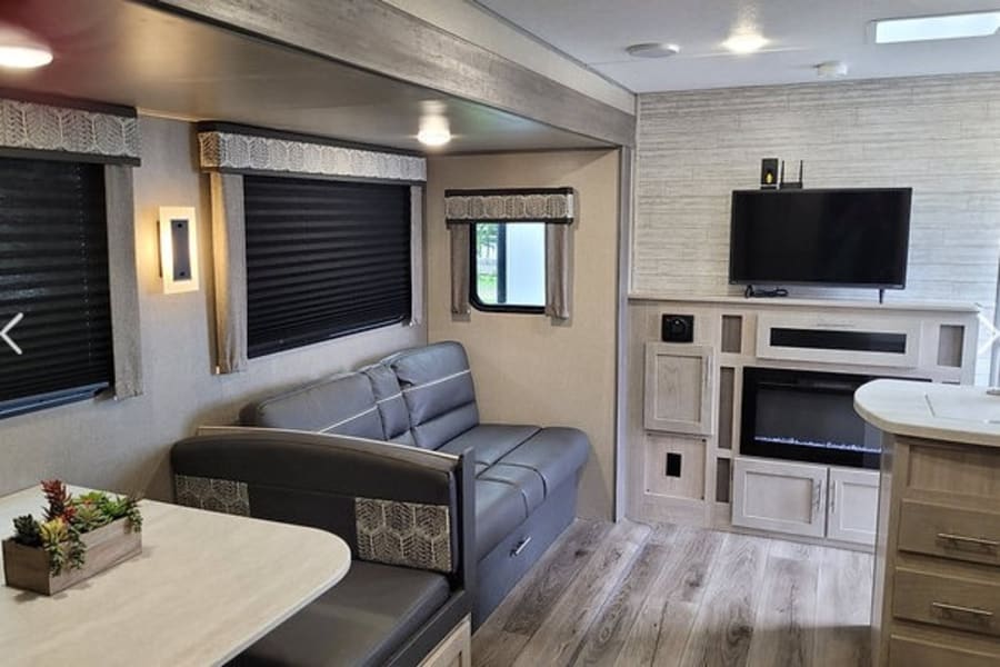 Inside this modern RV rental: a comfortable living space with dinette, sofa, TV, and cozy electric fireplace.