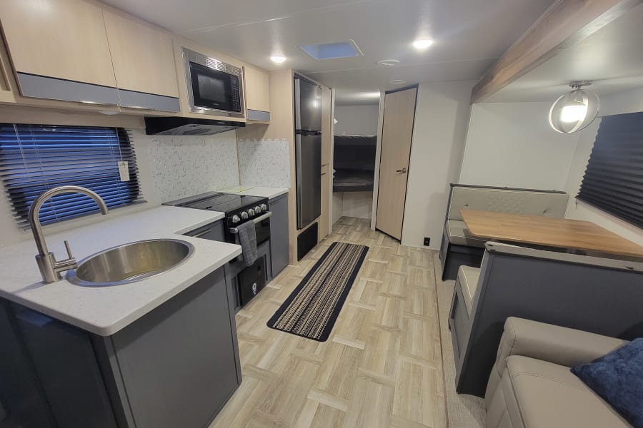 Well-lit rv rental interior with a full kitchen, dining area, lounge space, and bunk beds.