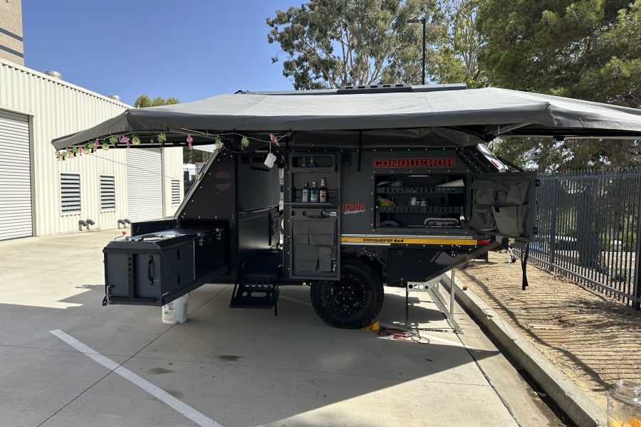 Explore with this robust Conqueror off-road camper. Perfect for rv rental, it features an outdoor kitchen & large awning setup.