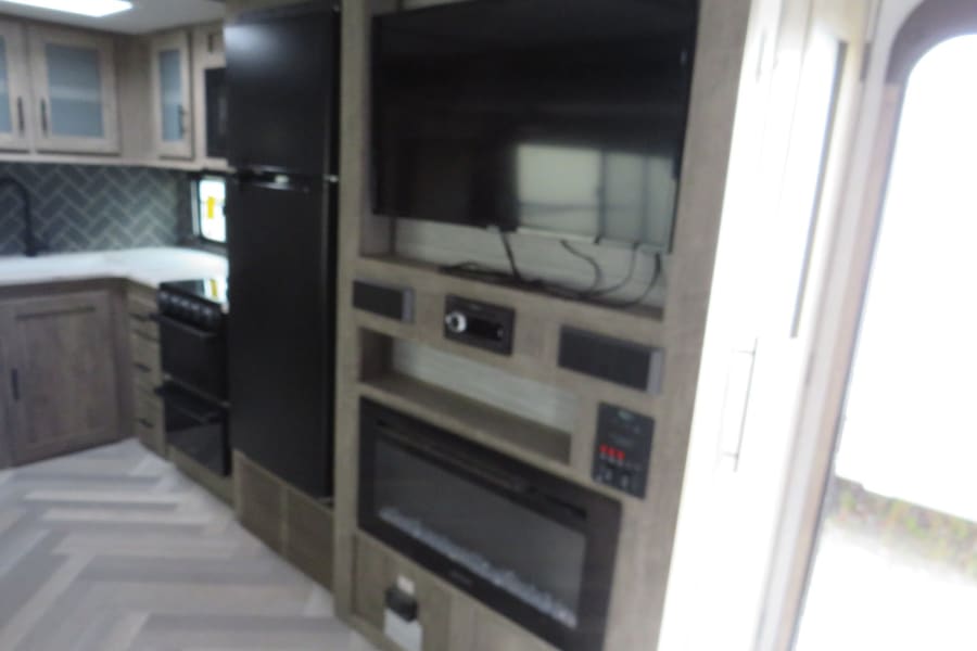 Modern RV rental interior with a fully equipped kitchen, TV, entertainment center, and electric fireplace.