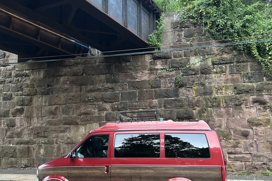 Red conversion van, like an RV rental, with wood trim parked by a stone wall under a bridge.