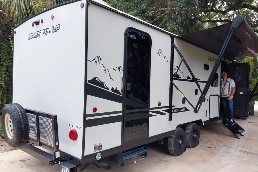 This Grey Wolf RV rental, with its extended awning, rear rack, and steps, offers outdoor adventure. A man stands by the door.
