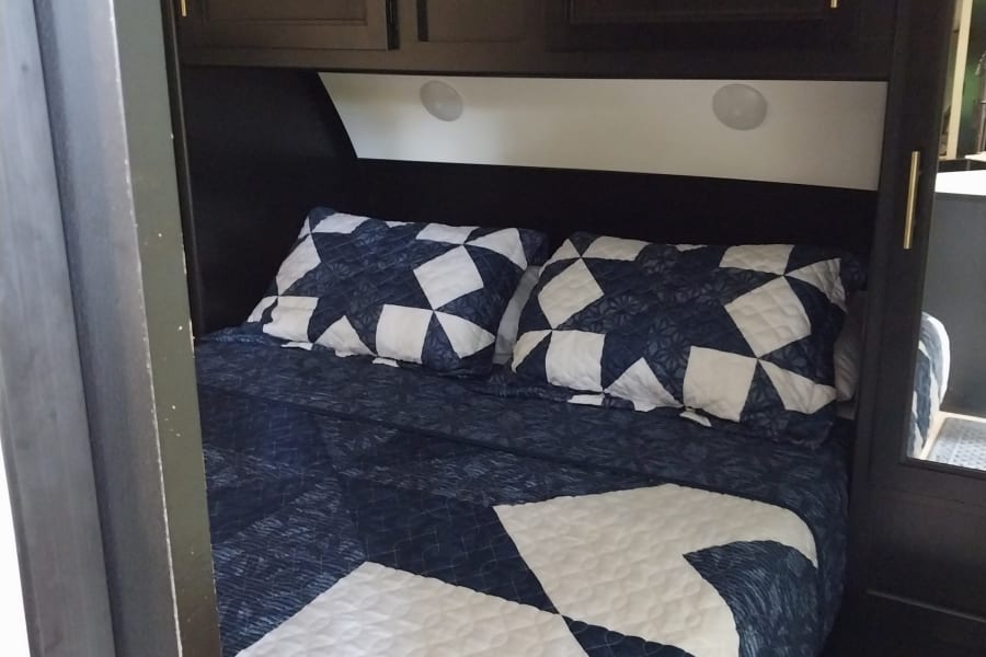 Cozy RV rental bedroom with patterned blue and white bedding, overhead storage, and integrated lighting for comfortable stays.
