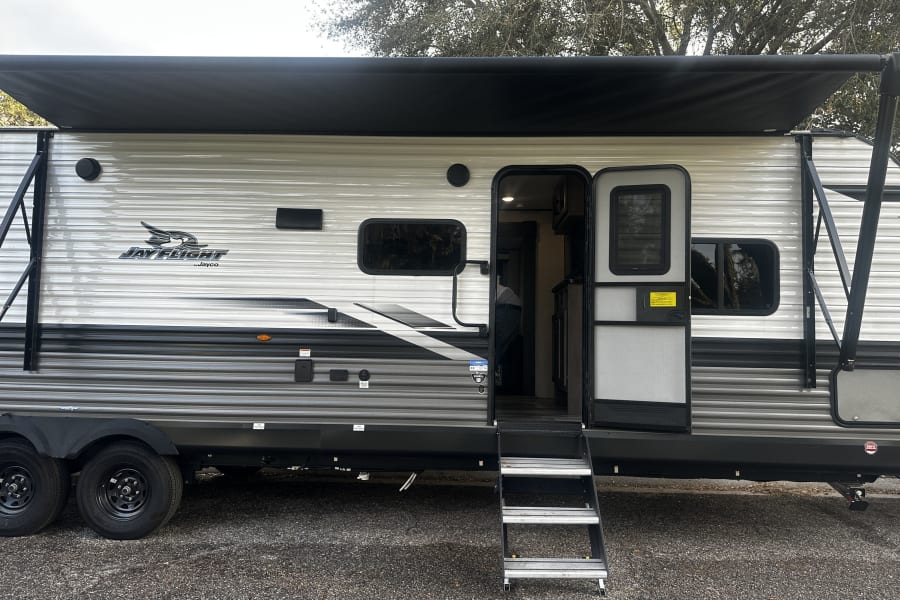 Jay Flight RV rental: a modern travel trailer with extended awning, open door, and steps, perfect for camping.