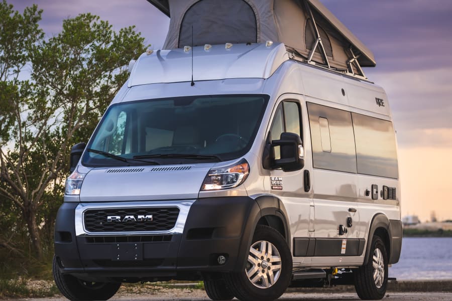 Silver Ram ProMaster pop-top camper van, perfect for an RV rental adventure, parked by the water at sunset.