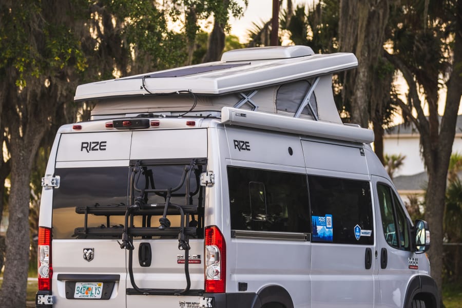 This sleek RIZE pop-top RV rental is ready for adventure with a bike rack and generator. Perfect for travel!