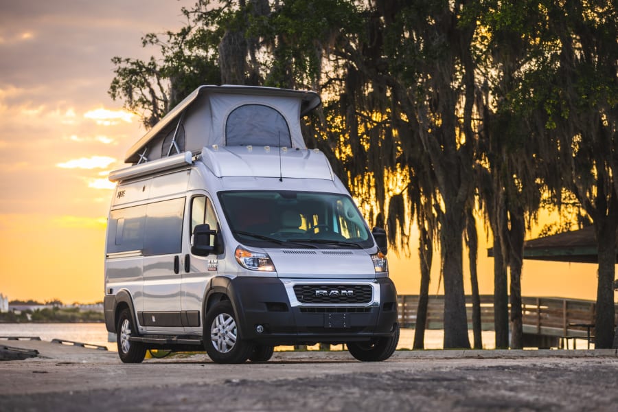 Silver pop-top rv rental parked at sunset beside mossy trees and water. Ideal for picturesque journeys.
