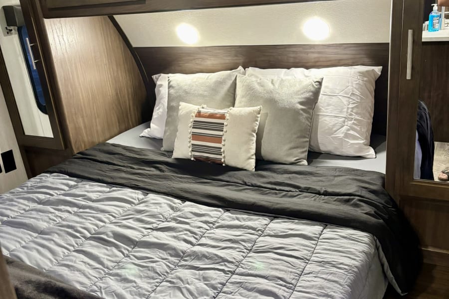 Cozy RV rental bedroom featuring dark wood overhead cabinets, bright reading lights, and comfortable bedding for travel comfort.